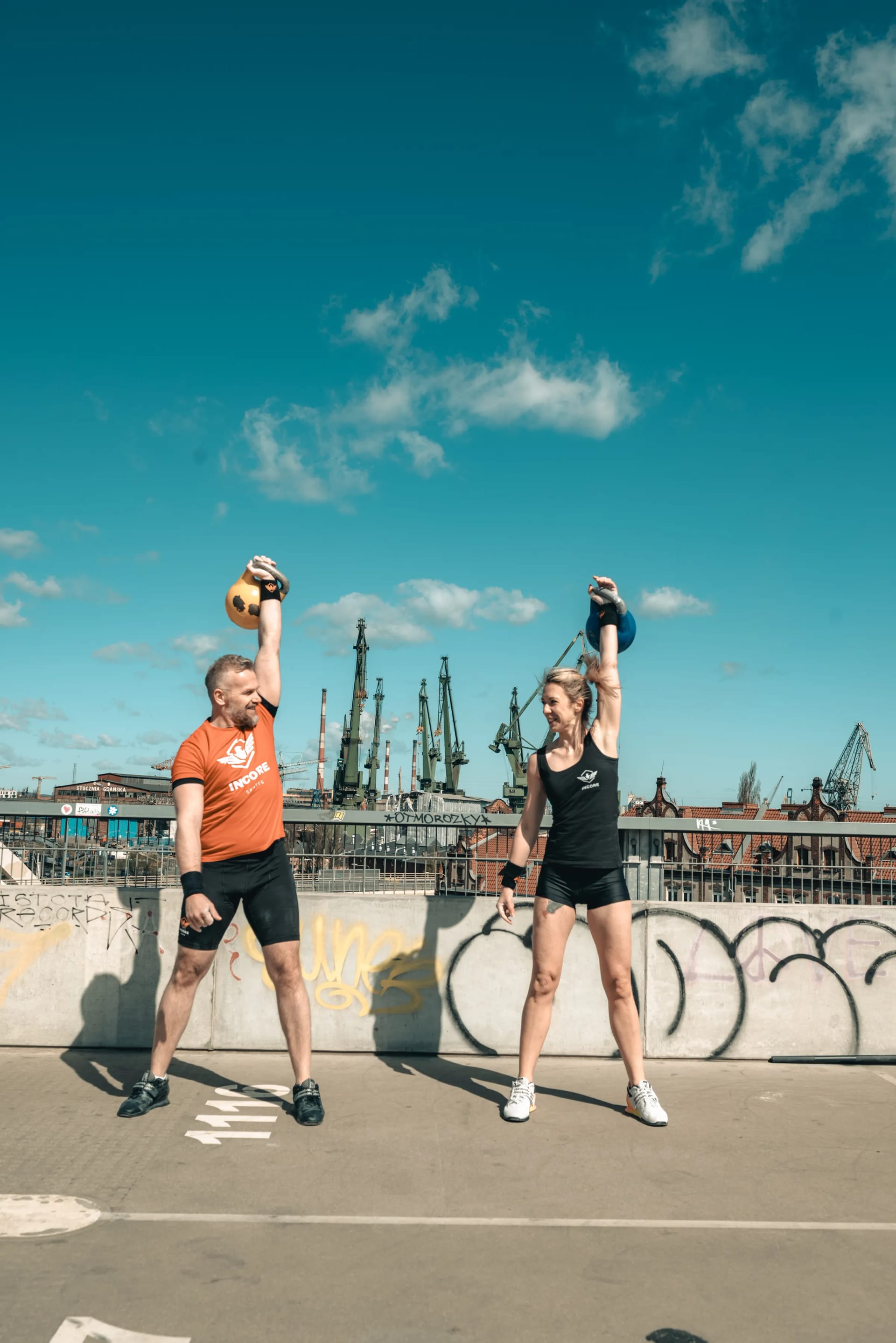 Two Incore Sports athletes pressing kettlebells overhead on a rooftop